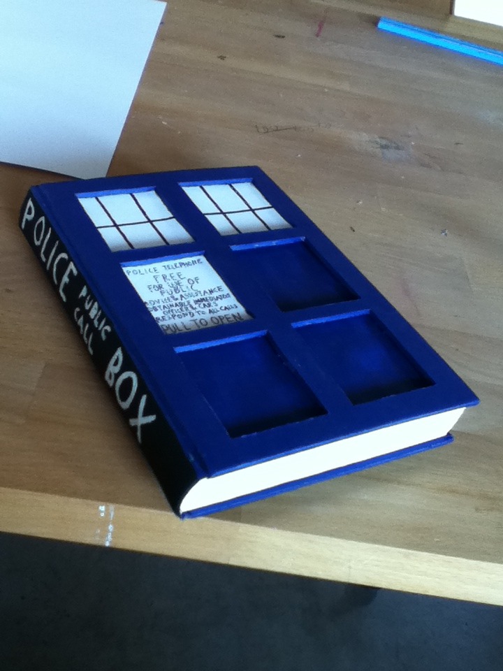 photo of a book cut and painted to look like the tardis from doctor who, police public call box is written along the spine