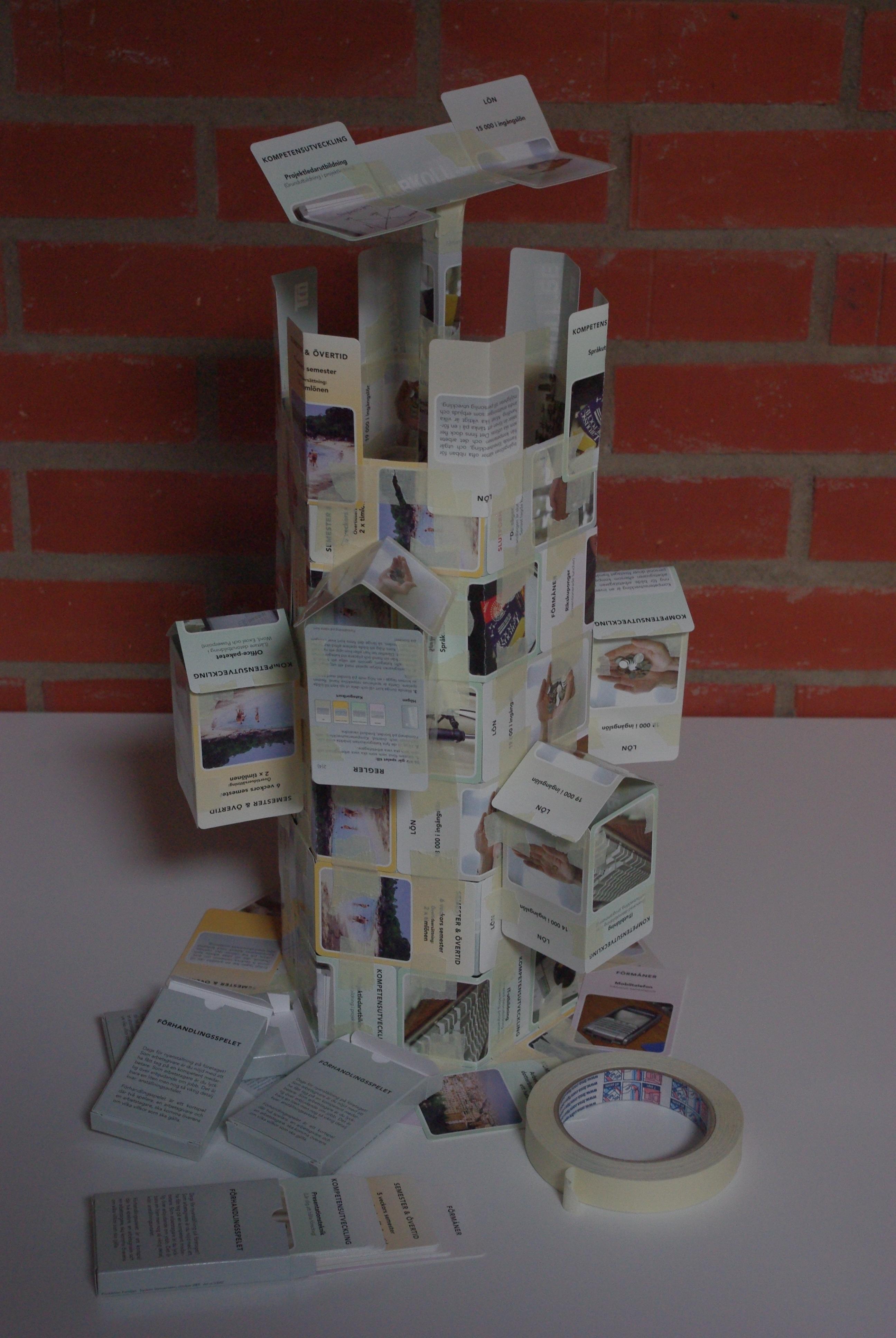 photo of a hexagonal tower made of cards and masking tape, there are outcroppings with triangular roofs around the walls, the top has crenellations and a kind of antenna thing